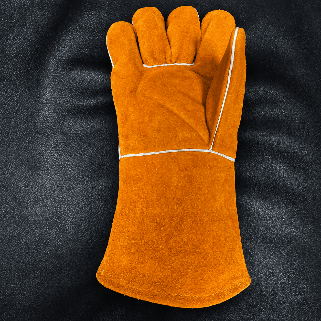 Ochre suede welding glove with white seams on a charcoal leather surface